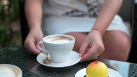 Close-up of a woman's hands holding a cup of coffee at an outdoor cafe, with a Vídeo Stock 285471996