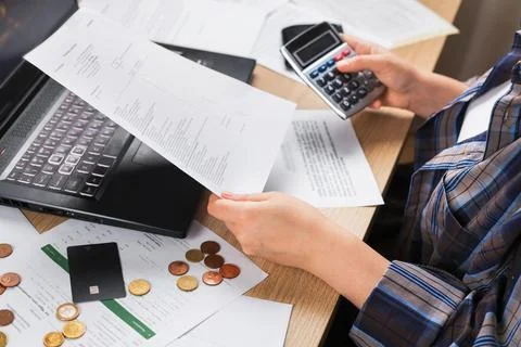 A close-up of a woman's hands holding documents and a calculator over a tab.. Stock Photos