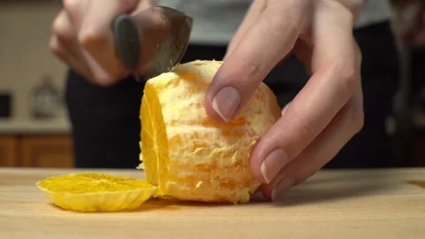 Close-up of a woman's hands in a home kitchen slicing a peeled orange. Stock Footage 148784012