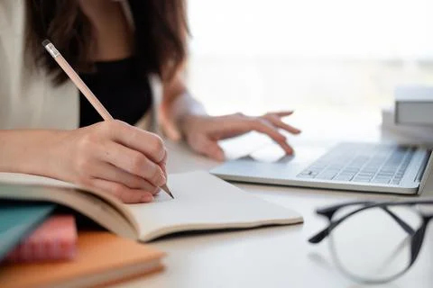 Close up woman's hands with laptop computer, notebook and pen taking notes in Stock Photos
