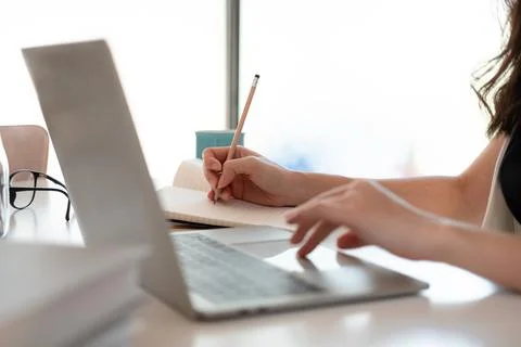 Close up woman's hands with laptop computer, notebook and pen taking notes in Stock Photos