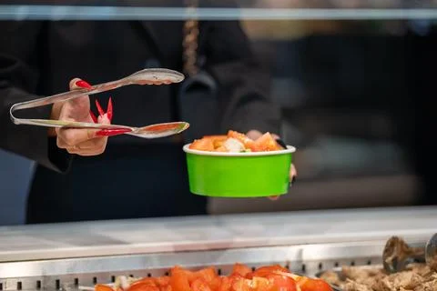 A close-up of a woman's hands with long red nails using metal tongs to serve  Fotos Stock