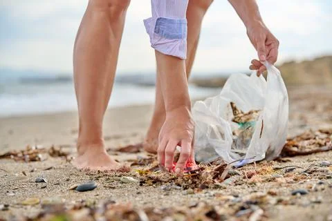 Close-up of a woman's hands picking up plastic trash into a bag on the beach Stock Photos