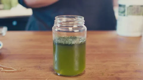 Close up of woman's hands preparing a green barley juice from powder using a jar Stock Footage 273510800