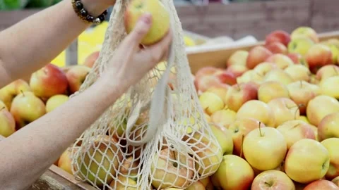 Close-up of woman's hands putting apples in mesh shopping bag Stock Footage 214207747