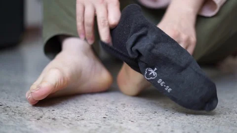 Close-up of woman's hands putting on black socks  on her feet. Woman wearing col Stockbeeldmateriaal 105382931