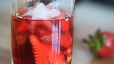 Close-up of the woman`s hands putting ice in a glass with strawberry tea. Stock Footage 91128734