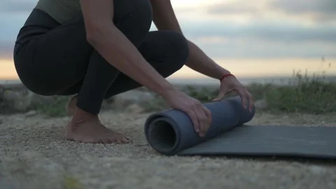 Close up of a woman's hands rolling up a yoga mat after an outdoor session. Stock Footage 219415558