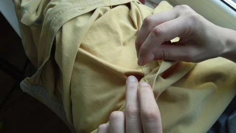 Close up woman's hands sewing a button to a yellow shirt. Female at work Stock Footage 137276880