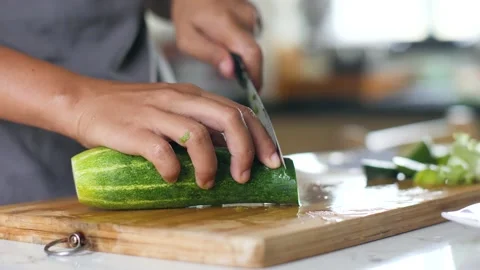 Close up of woman's hands slicing ca fresh cucumber on a wooden cutting board. Stock Footage 141348888