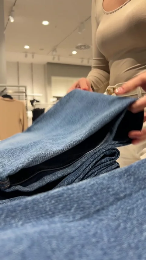 Close-up: womans hands sort through stack of jeans on clothing store shelf Stock Footage 289573223