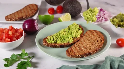 Close up of woman's hands spreading mashed avocado on slice of healthy toasts Stock Footage 136871900