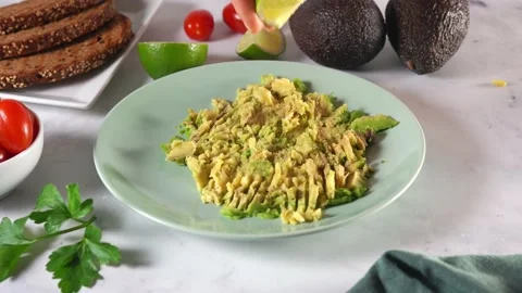 Close up of woman's hands squeezing a slice of lime on mashed avocado toast 스톡 동영상 136871738