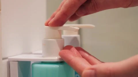 A close-up of a womans hands squeezing soap from a dispenser in a bathroom Stock Footage 332592425