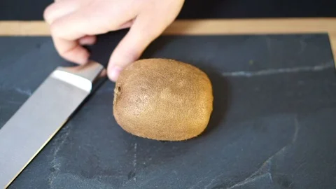 Close up, a woman's hands take a knife and cut the Kiwi exactly in half, Stock Footage 106761227