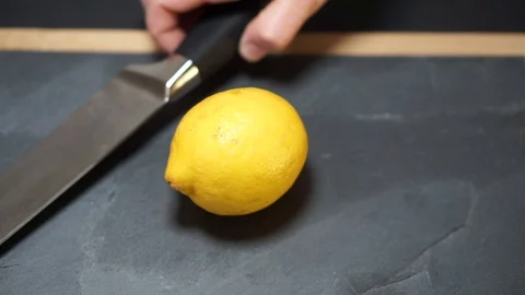 Close up, a woman's hands take a knife and cut the yellow lemon exactly in half, Stock Footage 106761435