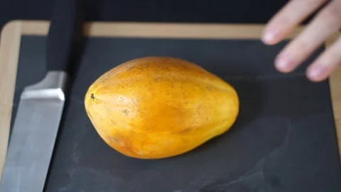 Close up, a woman's hands take a knife and cut the yellow Papaya exactly in half Stock Footage 106761510