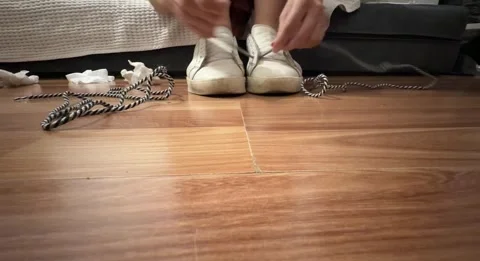 Close-up of a woman’s hands threading shoelaces through eyelets on worn white Stock Footage 337354966