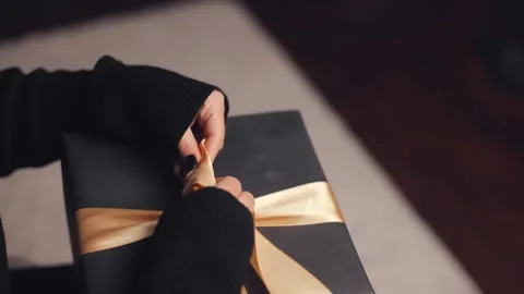 Close-up of a woman's hands tying a bow on a gift box in black and gold colors Video stock 253085316