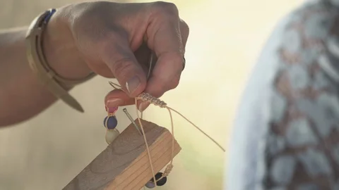 Close-up of a woman's hands tying a string with beads, making a jewelry bracelet Stock Footage 119646831