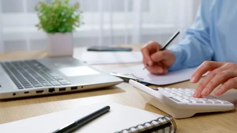 Close-up of a woman's hands using a calculator and writing on an office desk.  Видео 329557531