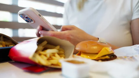 Close-up of a woman's hands using her mobile phone while eating a hamburger.. Stock Footage 342167443