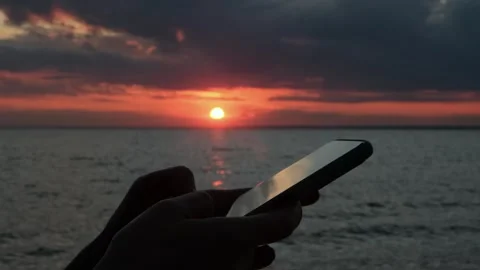 Close-up of a woman's hands using a smartphone standing by the sea at sunset. Stock Footage 309637418
