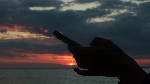 Close-up of a woman's hands using a smartphone standing by the sea at sunset. Stock Footage 310579502