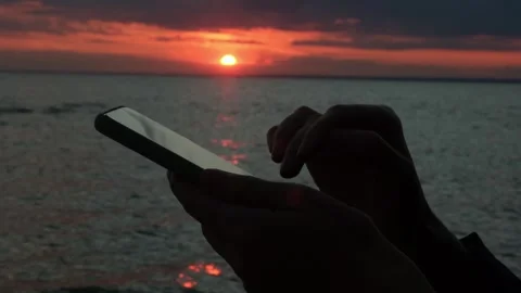 Close-up of a woman's hands using a smartphone standing by the sea at sunset. Stock Footage 311701153