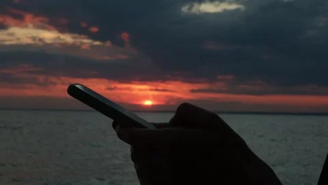 Close-up of a woman's hands using a smartphone standing by the sea at sunset. Stock Footage 314971188