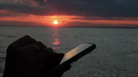 Close-up of a woman's hands using a smartphone standing by the sea at sunset. Stock Footage 315588002