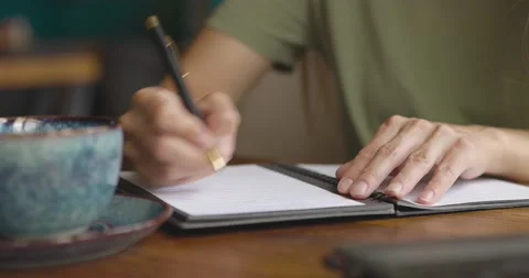 Close up of woman's hands writing down on a paper notebook with coffee cup and Video stock 158958139