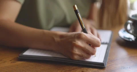 Close up of woman's hands writing down on a white blank notebook with cup on Stock Footage 159012068