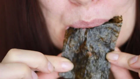 Close-up of a woman's mouth as she eats, bites and chews crunchy seaweed sheets Stock Footage 260694306