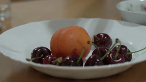 Close-up of women's hands pulling red cherries out of a white plate against a Stock Footage 198361604