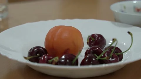Close-up of women's hands pulling red cherries out of a white plate against a Stock Footage 198361698