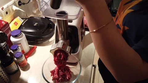 Close-up women's hands putting beef and pork meat and onion through mincer at Stock Footage 100044075