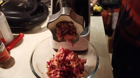 Close-up women's hands putting beef and pork meat and onion through mincer at Stock Footage 100044733