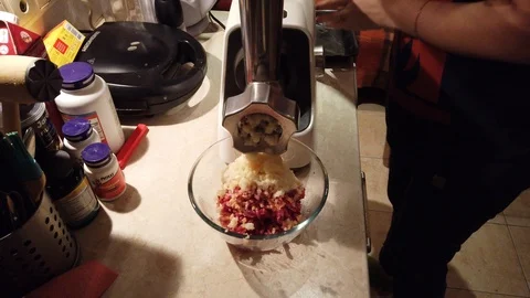 Close-up women's hands putting beef and pork meat and onion through mincer at Stock Footage 100045443
