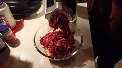Close-up women's hands putting beef and pork meat and onion through mincer at Stock Footage 100045762