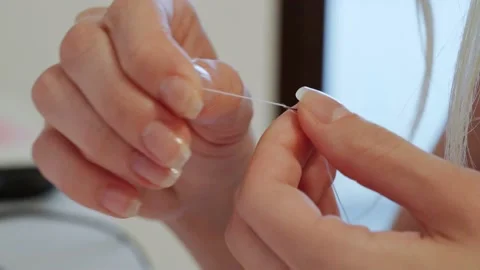 Close-up of women's hands threading a white thread into the little eye of a Stock Footage 201676335
