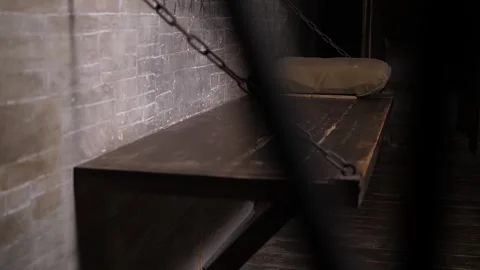 A close-up of a wooden bed hanging on chains in an old prison cell. Stockbeeldmateriaal 291516616