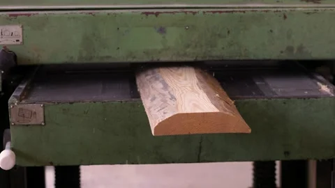 A close-up of a wooden board being processed in a green industrial planer Stock Footage 296042656