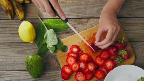 Close-up wooden kitchen table, cutting board, hands are slicing strawberries 動画素材 246536891