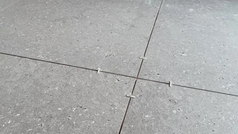 Close-up of a worker adjusting white spacers between large gray floor tiles Stock Footage 345068020