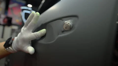 Close up of a worker applying matte vinyl wrap on a car body panel in a Stock Footage 334056393