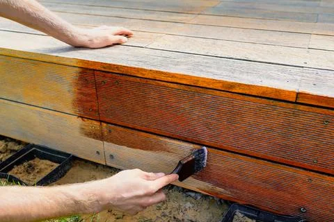 Close-up of a worker applying stain and protective coating to a wooden deck.. 스톡 사진