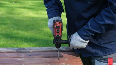 A close-up of a worker in a blue jacket and protective gloves drilling a hole Stock Photos