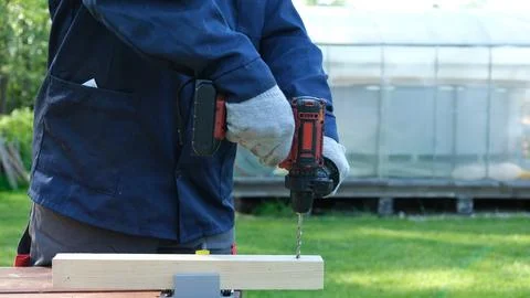 Close-up of a worker in a blue jacket and protective gloves using a cordless Stock Photos