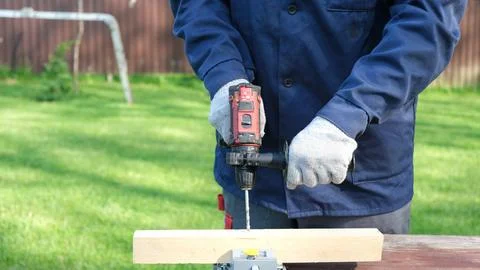 Close-up of a worker in a blue jacket and protective gloves using a cordles.. Stock Photos